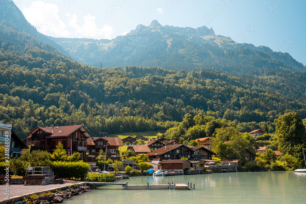 View of Brienz lake with clear turquoise water. Sailing boats. Traditional wooden houses on the shore of Brienz lake in the village of Iseltwald, Switzerland