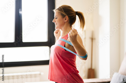 beautiful blonde caucasian athlete woman doing exercises with elastic band in living room at home © Dani