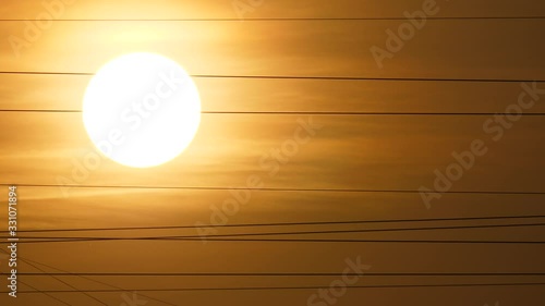 Large and bright sun disc, thin optical Fiber optic cable lines across sky, telephoto perspective. Glowing halo around sundisk. Optical telecommunication or high-speed internet data transfer cables photo