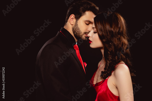 Side view of handsome man kissing elegant girlfriend isolated on black