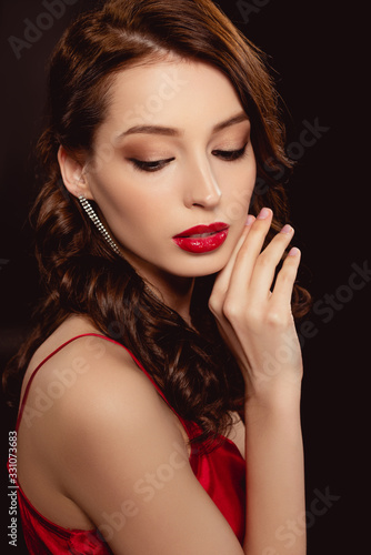Side view of attractive brunette woman with red lips and hand near face isolated on black