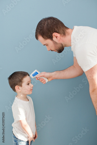 young man is measuring body temperature of a toddler boy