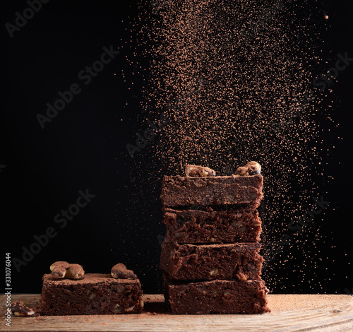 Fotografía stack of square baked brownie pieces sprinkled with cocoa powder, particles froz