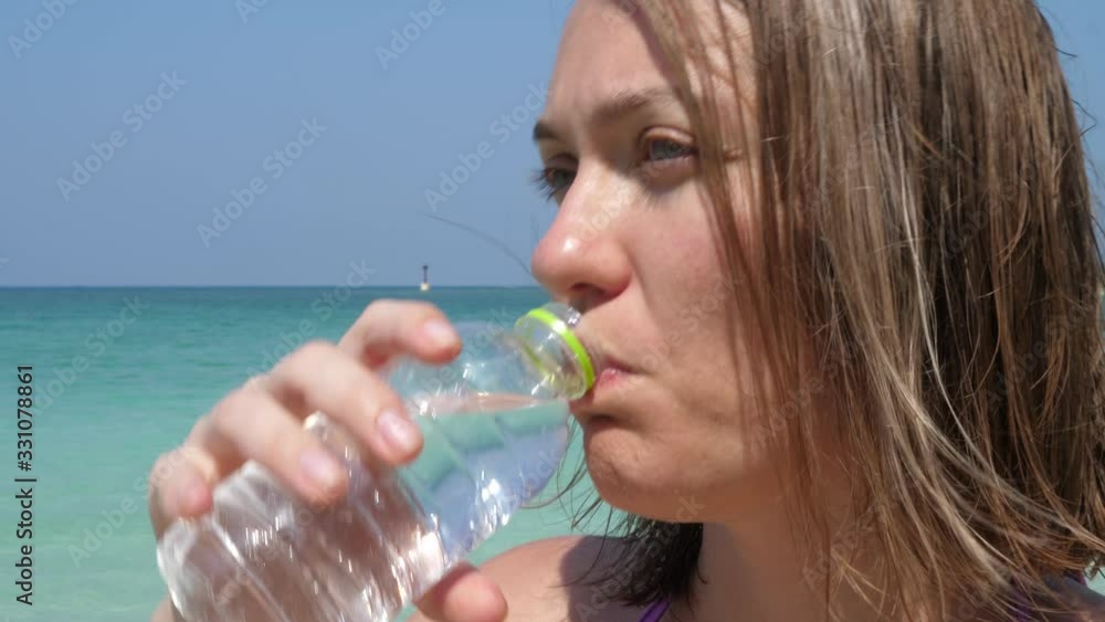 Attractive Woman Drink Refreshment beverage Water in bottle on beach in hot time. Wave Sea Surface at Sunny Summer Day. Healthy beautiful young woman outdoor Attractive Woman Drink Refreshment beverage Water in bottle on beach in hot time. Wave Sea Surface at Sunny Summer Day. Healthy beautiful young woman outdoor