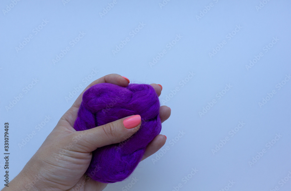 Woman's hand with pink manicure holding a piece of violet wool on white background. Concept of felting creative hobby. Woman's hand with pink manicure holding a piece of violet wool on white background. Concept of felting creative hobby.