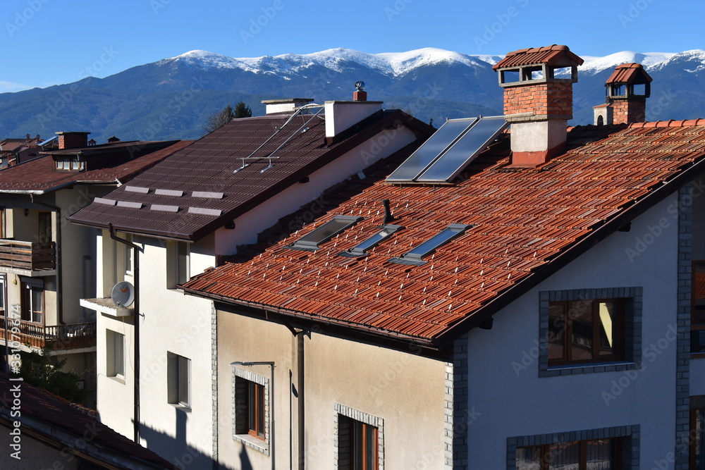 Breathtaking snowy mountain views over tiled rooftops of stone houses lined up a street in Bansko town Once small quaint village in the Pirin National Park it transformed to first class winter resort