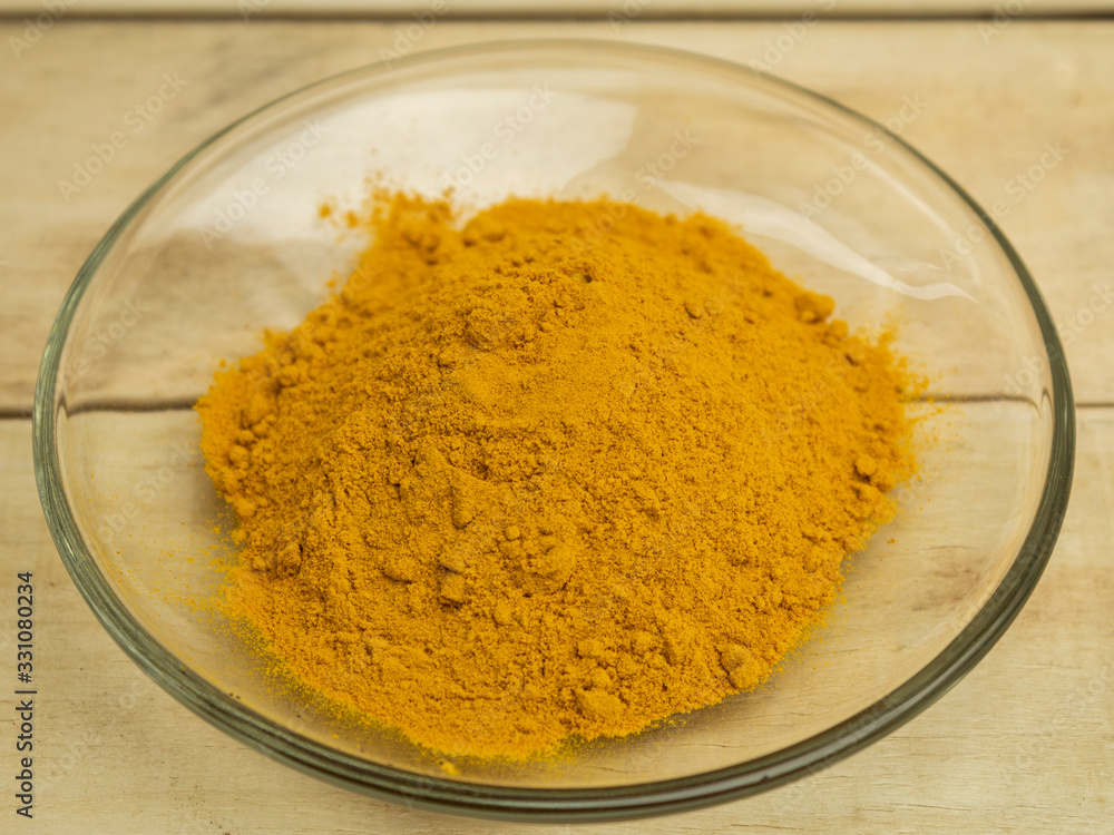 Turmeric powder seasoning in glass plate on wooden background Turmeric powder seasoning in glass plate on wooden background