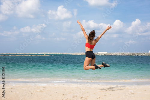 Fitness woman jumping on the beach with arms out on a sunny day