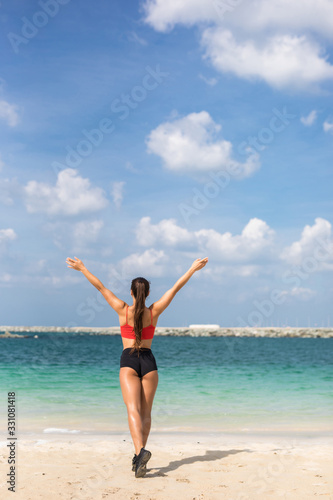 Rear view portrait of fitness woman stretching with her hands raised at the beach