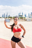 Fitness selfie woman self portrait after workout. Sport athlete taking selfies photo on the phone after working out running and training outdoors on beach. Fit female sport model smiling happy.