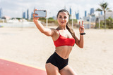 Smiling beautiful young fitness woman take a selfie by mobile phone outdoors on beach