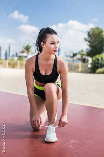 Young fitness girl tying shoelaces on the beach