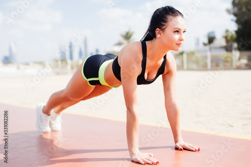 Side view of beautiful fitness woman in plank position on the beach