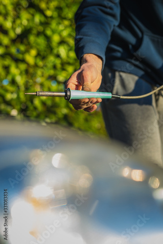 Man soldering wires in a car engine compartment. Modern car with repairs being done by a home mechanic. Caucasian holding a professional wire welder.