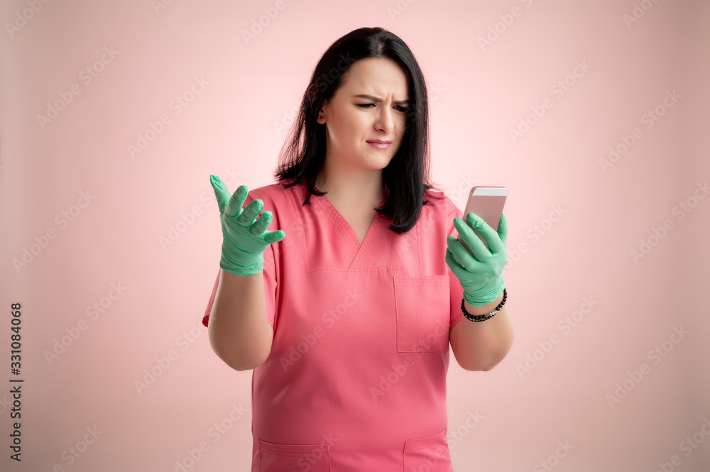 Beautiful woman doctor with stethoscope, wearing pink scrubs holding smartphone, texting, looking nervously Beautiful woman doctor with stethoscope, wearing pink scrubs holding smartphone, texting, looking nervously