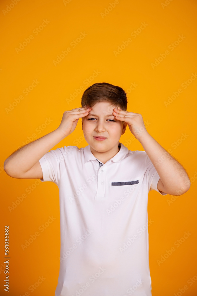 A boy with a headache. Caucasian child on a yellow background suffering from headache and migraine. Hands on the head. A boy with a headache. Caucasian child on a yellow background suffering from headache and migraine. Hands on the head.