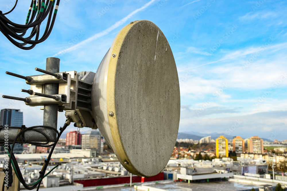 Micro wave radio telecommunication network dish antenna mounted on a metal pole providing transmission strong signal waves from the top of the roof connecting multiple base station across the city