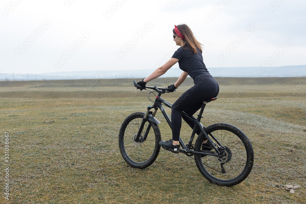 Girl on a mountain bike on offroad, beautiful portrait of a cyclist in rainy weather, Fitness girl rides a modern carbon fiber mountain bike in sportswear. Close-up portrait of a girl in red bandana. Girl on a mountain bike on offroad, beautiful portrait of a cyclist in rainy weather, Fitness girl rides a modern carbon fiber mountain bike in sportswear. Close-up portrait of a girl in red bandana.