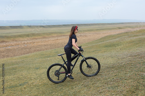 Girl on a mountain bike on offroad  beautiful portrait of a cyclist in rainy weather  Fitness girl rides a modern carbon fiber mountain bike in sportswear. Close-up portrait of a girl in red bandana.