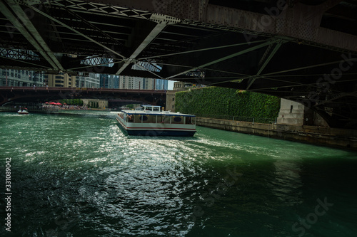 Sightseeing boat traveling on the Chicago river seen as it passes from under a steel bridge.