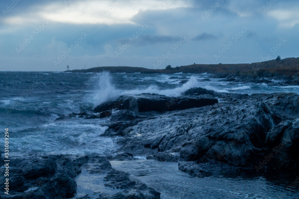 Small waves hitting black rocks with cloudy sky