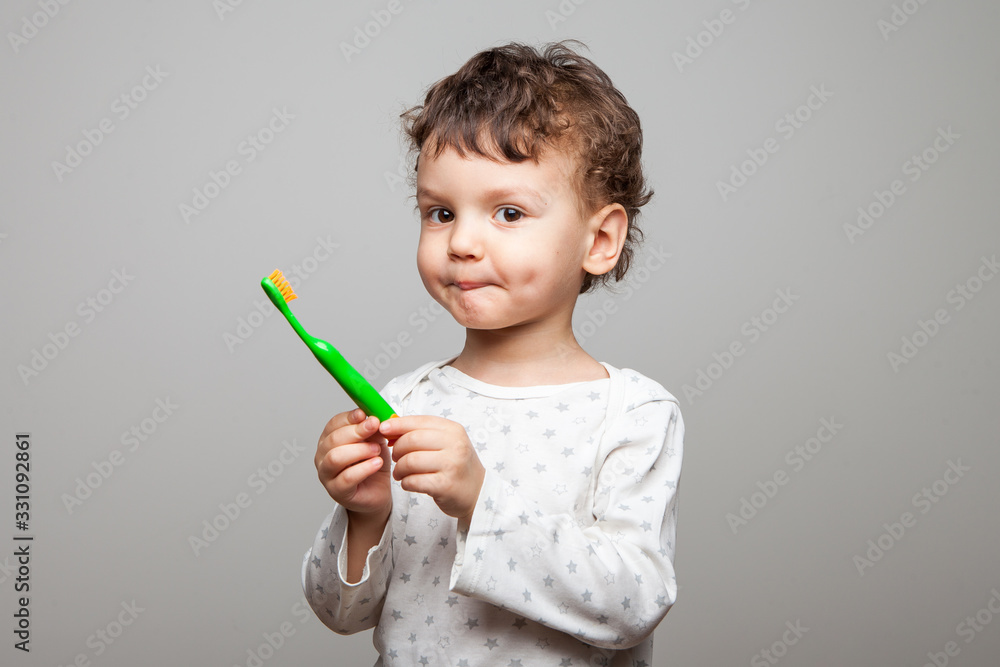 funny boy, curly and cute baby with a grimace on his face holds a toothbrush in his hands. hygiene procedures in the morning and at bedtime. teeth cleaning. healthy strong teeth. studio, isolated, funny boy, curly and cute baby with a grimace on his face holds a toothbrush in his hands. hygiene procedures in the morning and at bedtime. teeth cleaning. healthy strong teeth. studio, isolated,