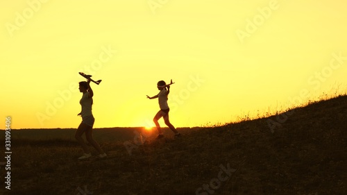 Dreams of flying. Silhouette of children playing on plane. Children run from mountain with an airplane in hand at sunset. Happy childhood concept. girls play with a toy plane at sunset.