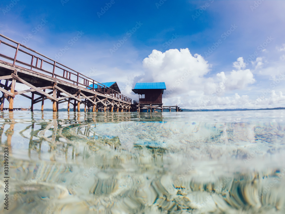 Picturesque landscape of seascape with touristic bungalow with pier walkway over oceanic crustal water, beautiful tropical nature environment for recreation during summer vacation in New Guinea