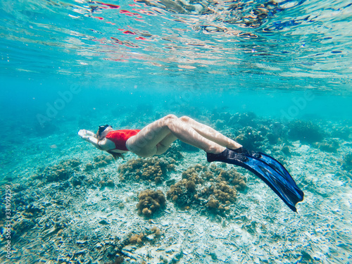 Young woman snorkeling in sea water above corals