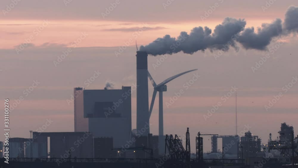 Coal power plant with a smoking chimney next to a spinning wind turbine. Long shot by sunset. Coal power plant with a smoking chimney next to a spinning wind turbine. Long shot by sunset.