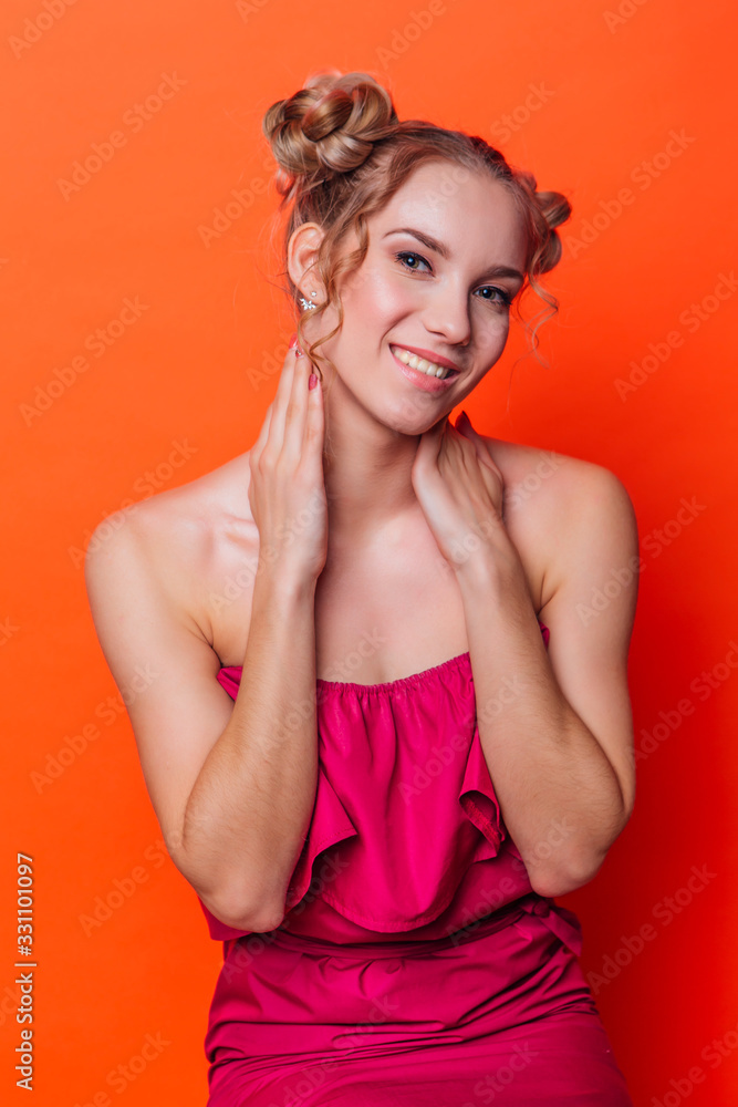 The girl in a red dress on a orange background in the studio. Blonde girl with two hair knots looking to the camera and smiling. The girl in a red dress on a orange background in the studio. Blonde girl with two hair knots looking to the camera and smiling.