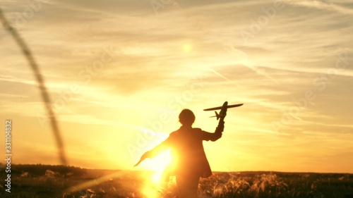 girl wants to become pilot and astronaut. Slow motion. Happy girl runs with a toy airplane on field in the sunset light. children play toy airplane. teenager dreams of flying and becoming pilot.