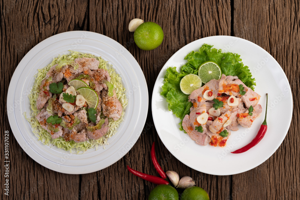 Spicy lime pork with salad, galangal, chilli, tomato and garlic on a white plate on a wooden floor. Spicy lime pork with salad, galangal, chilli, tomato and garlic on a white plate on a wooden floor.