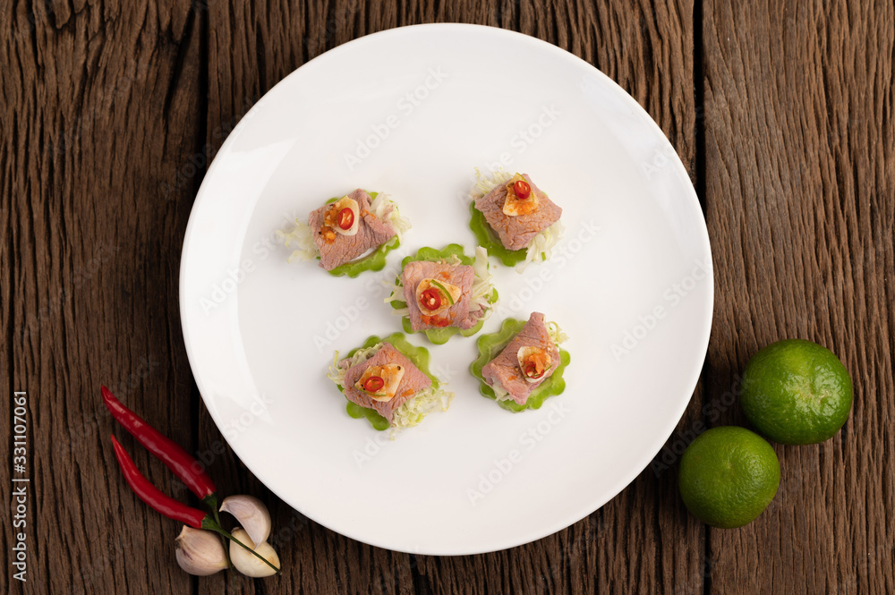 Spicy lime pork salad with bitter melon, galangal, chili, tomatoes and garlic in a white plate on a black cement floor.