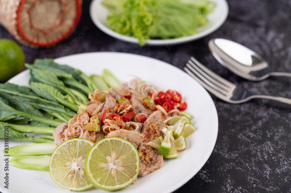 Spicy lime pork salad with kale, galangal, chilli and garlic in a white plate on a black cement floor. Spicy lime pork salad with kale, galangal, chilli and garlic in a white plate on a black cement floor.