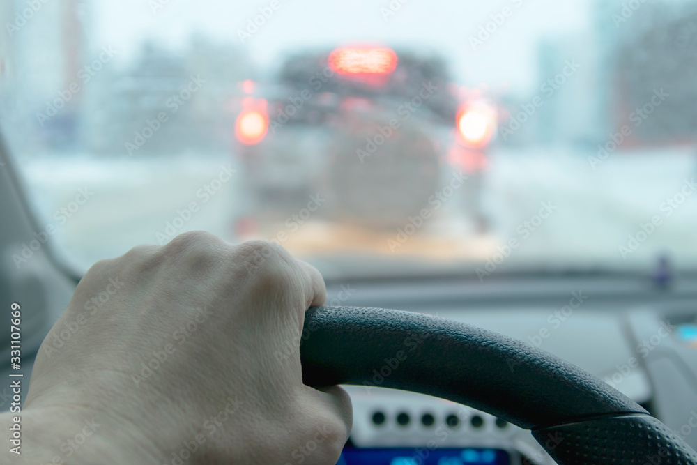 Hand holds the steering wheel of a car. Bad weather conditions. Signal lights of the car. Hand holds the steering wheel of a car. Bad weather conditions. Signal lights of the car.