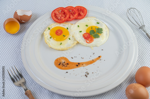 Fried egg on a white plate with sliced ​​Spring onion and sliced ​​tomatoes