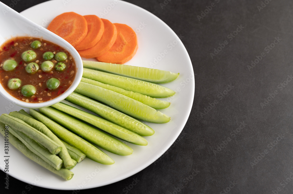 Shrimp-paste sauce in a bowl on the white plate with cucumber, yard long bean and carrots. Shrimp-paste sauce in a bowl on the white plate with cucumber, yard long bean and carrots.