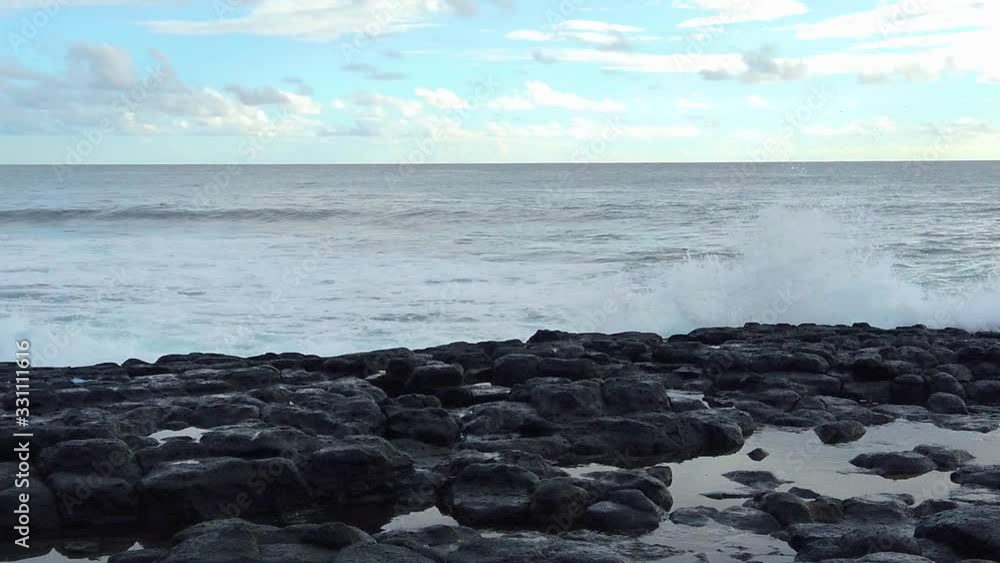 HD Slow motion Hawaii Kauai static of ocean waves splash high into frame as waves build toward camera with pools in lava rocks in foreground with partly cloudy sky HD Slow motion Hawaii Kauai static of ocean waves splash high into frame as waves build toward camera with pools in lava rocks in foreground with partly cloudy sky