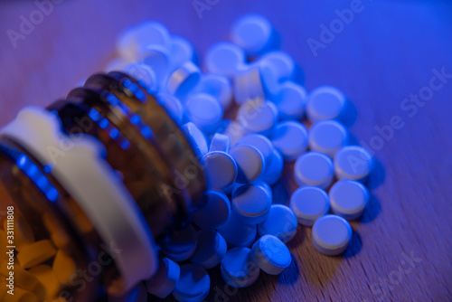 Bottle with pills on a table under blue light. Medication. Pharmaceuticals in a glass bottle on wooden surface