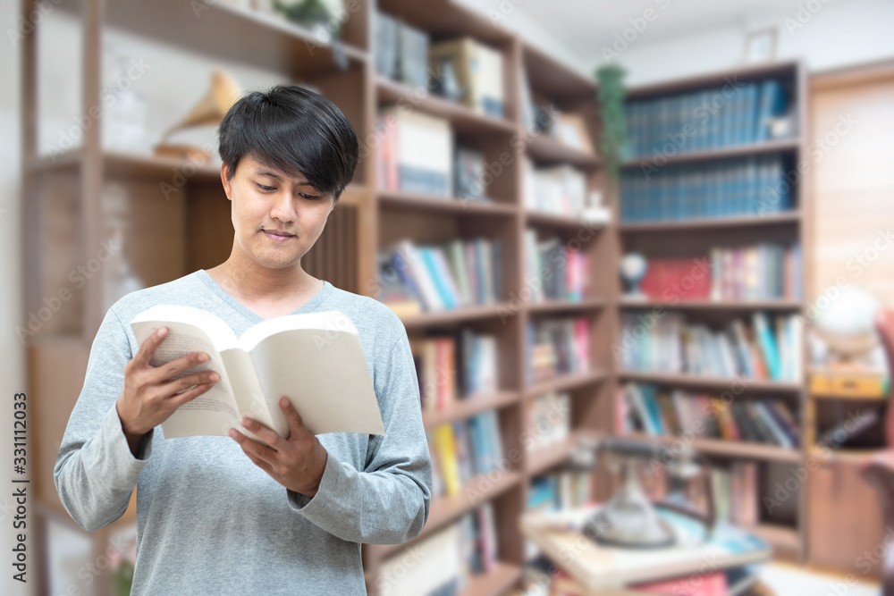 World book day concept.Young Asian man university student reading book sitting by bookshelf in college library for education research and self improvement. Scholarship and educational opportunity. World book day concept.Young Asian man university student reading book sitting by bookshelf in college library for education research and self improvement. Scholarship and educational opportunity.