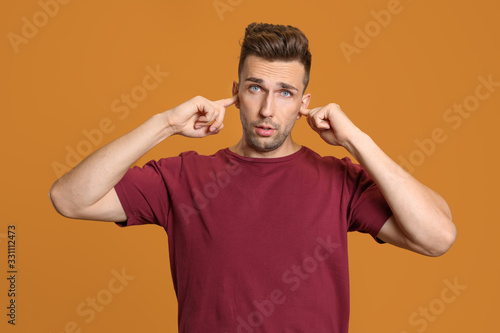 Young man closing ears with hands on color background © Pixel-Shot