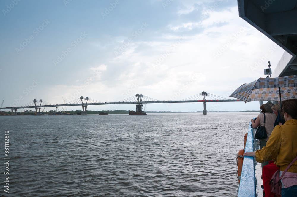 Russia, Blagoveshchensk, July 2019: people with umbrellas look at the bridge on the Amur river from Blagoveshchensk to the Chinese city of Heihe in summer from a pleasure boat