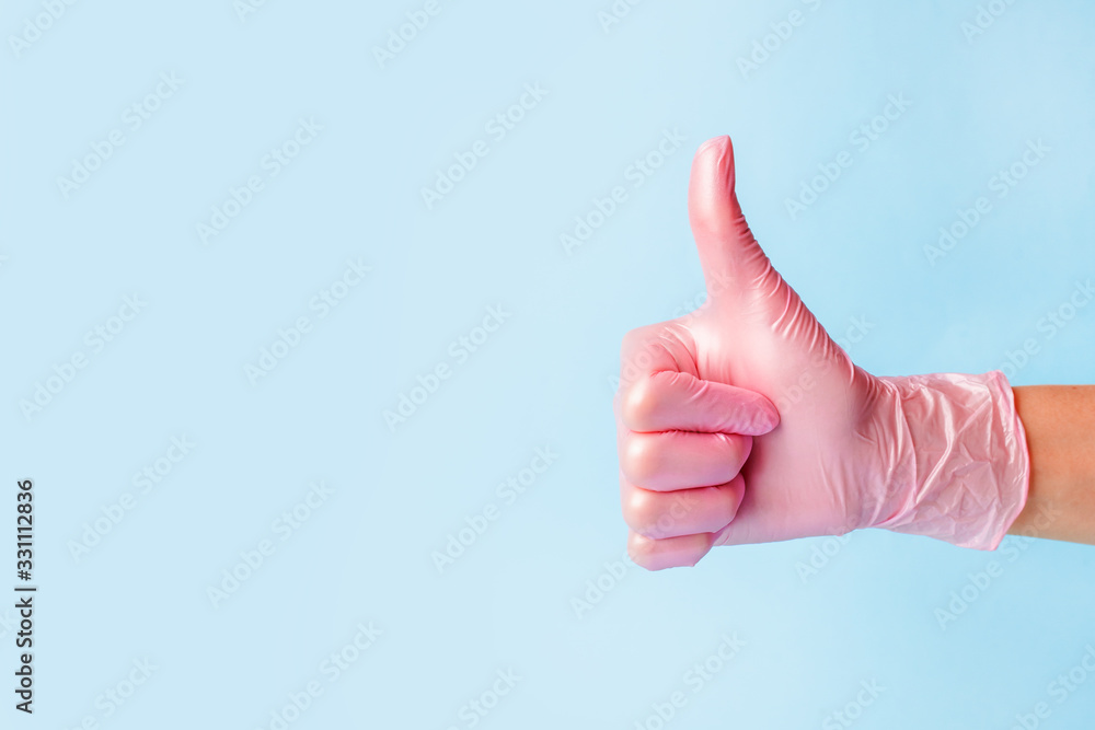 Closeup of female hand in pink cosmetic medical hygiene pharmacy gloves showing thumbs up sign against pastel blue background, copy space, minimal concept Closeup of female hand in pink cosmetic medical hygiene pharmacy gloves showing thumbs up sign against pastel blue background, copy space, minimal concept