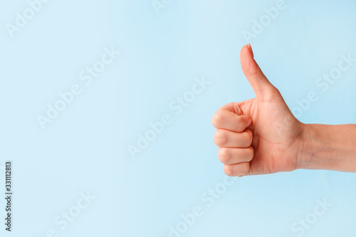 Cuadro en lienzo Closeup of female hand showing thumbs up sign against pastel blue background, co