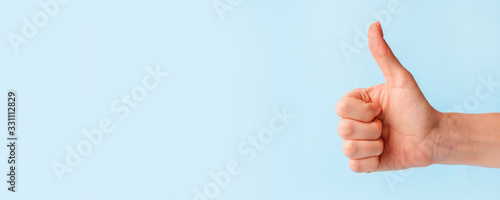 Closeup of female hand showing thumbs up sign against pastel blue background, copy space, minimal concept photo