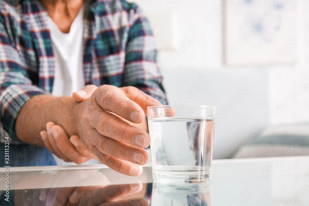 Senior man with Parkinson syndrome taking glass of water from table, closeup Senior man with Parkinson syndrome taking glass of water from table, closeup