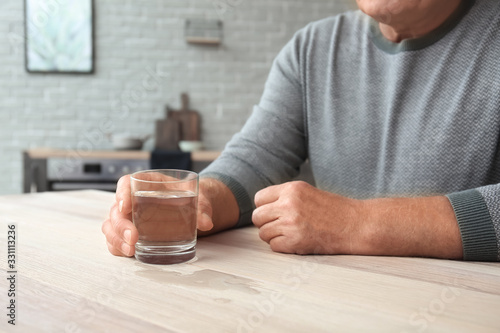 Senior man suffering from Parkinson syndrome with glass of water at home