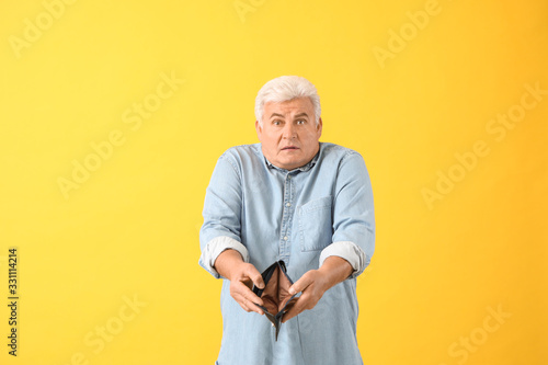 Sad senior man with empty purse on color background