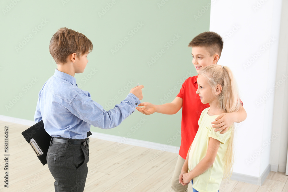 Little real estate giving a key from new house to clients indoors Little real estate giving a key from new house to clients indoors